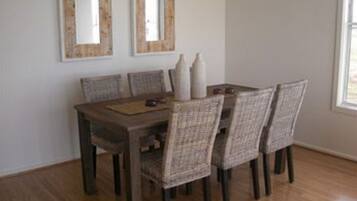 A dining area with a wooden table and six wicker chairs. There are two wall-mounted mirrors above the table.