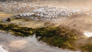 Une ville côtière dont le centre est constitué d’un ensemble de bâtiments blancs, entourés de verdure et bordée d’une plage de sable.