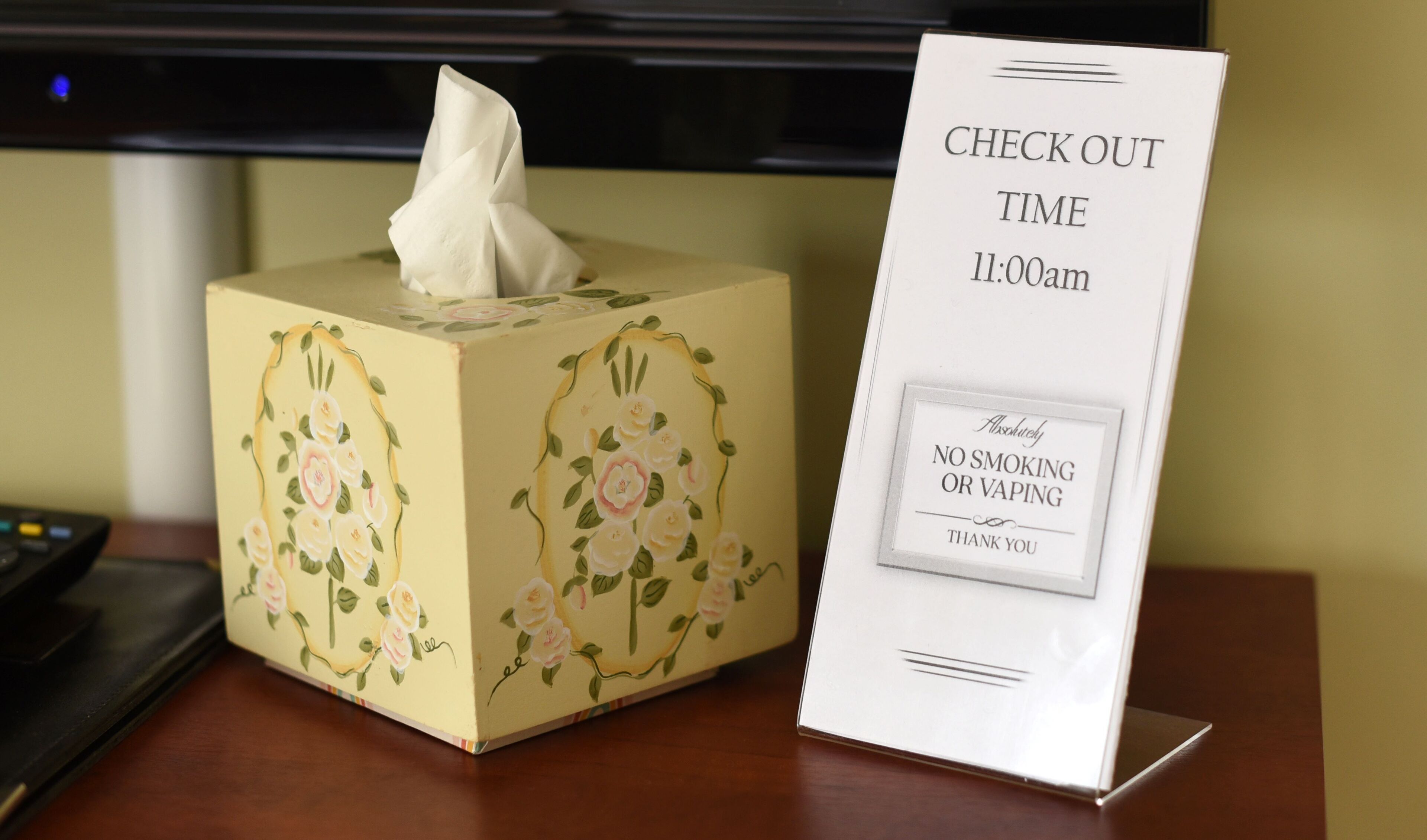 A tissue box with floral designs and a sign indicating check-out time and no smoking policy.