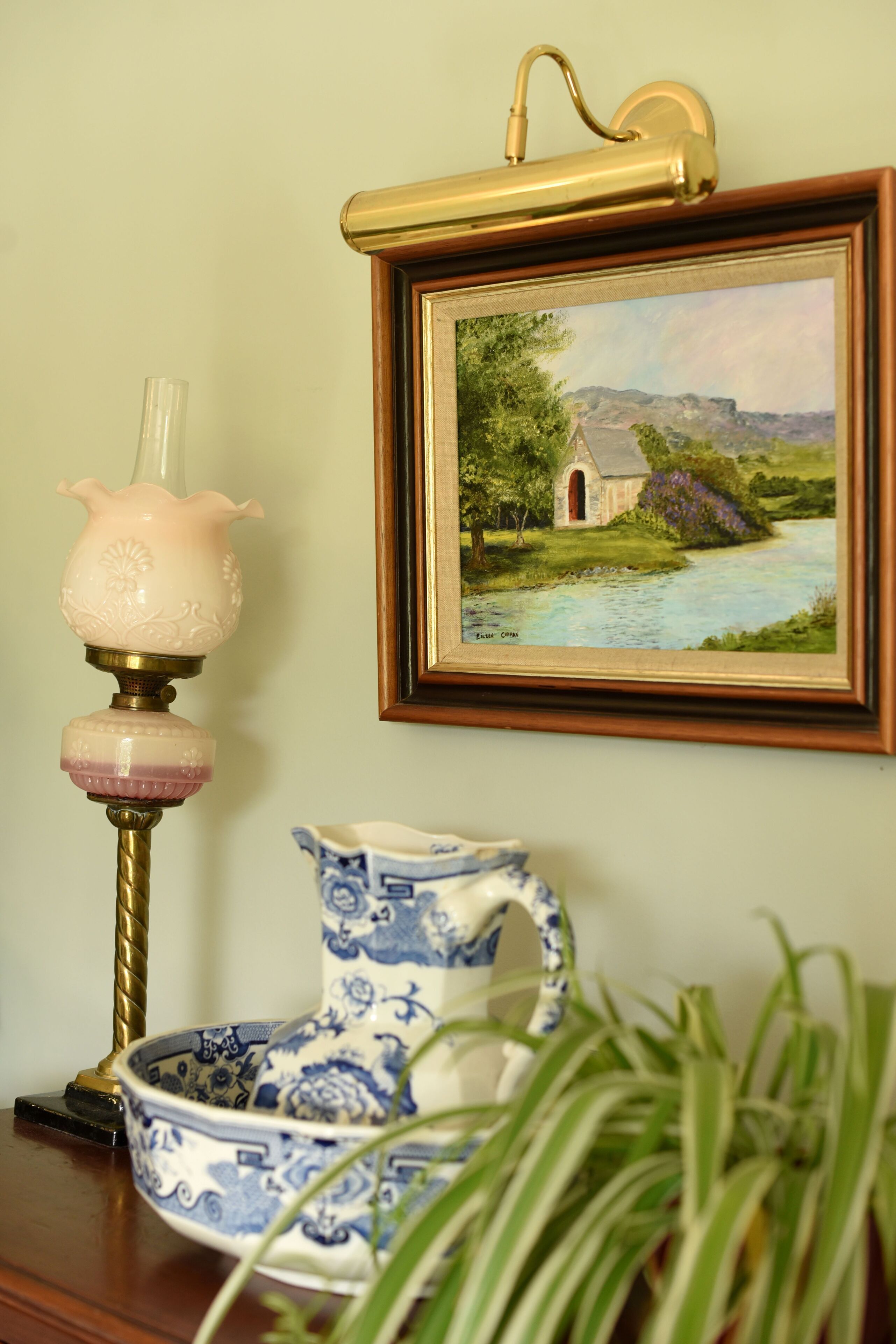 A framed landscape painting, a decorative lamp, and a blue and white ceramic pitcher on a wooden surface.