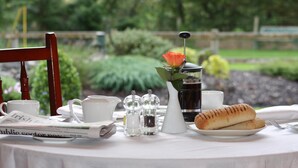 Une table dressée avec un journal, des tasses, des salières et des poivrières, un pichet, un verre de thé glacé et du pain.
