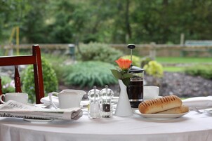 A table set with a newspaper, cups, salt and pepper shakers, a pitcher, a glass of iced tea, and bread.
