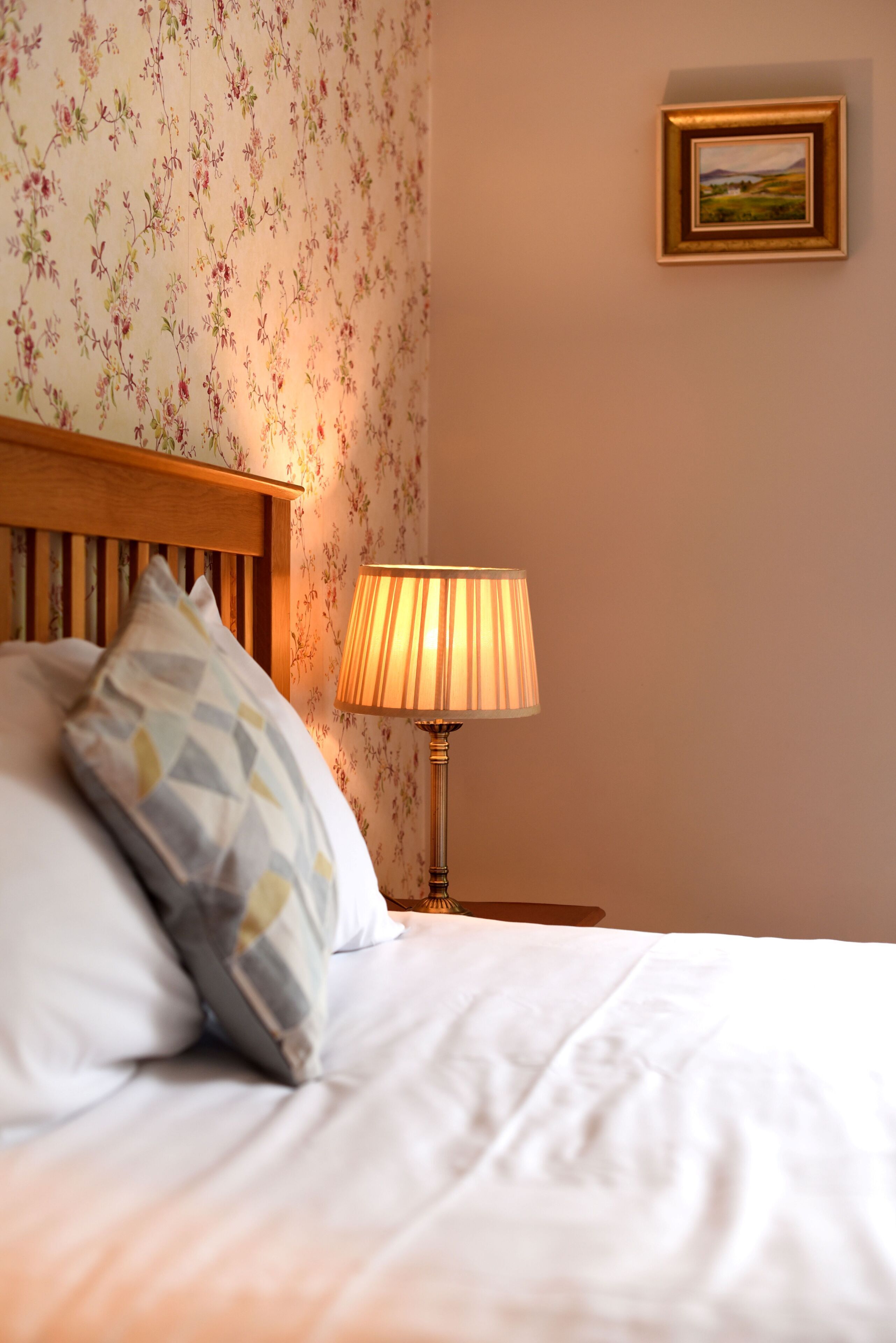 A neatly made bed with pillows, a wooden headboard, a lamp, and a framed picture on the wall.