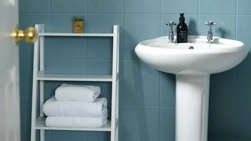 A bathroom with a white pedestal sink, a white shelf with folded towels, and a small potted plant on the wall.