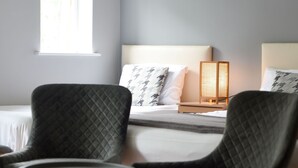 Une chambre à coucher moderne avec un lit, deux fauteuils, une petite table ronde et une lampe de chevet.