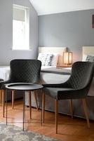 Un dormitorio moderno con una cama, dos sillones, una mesita redonda y una lámpara de noche.