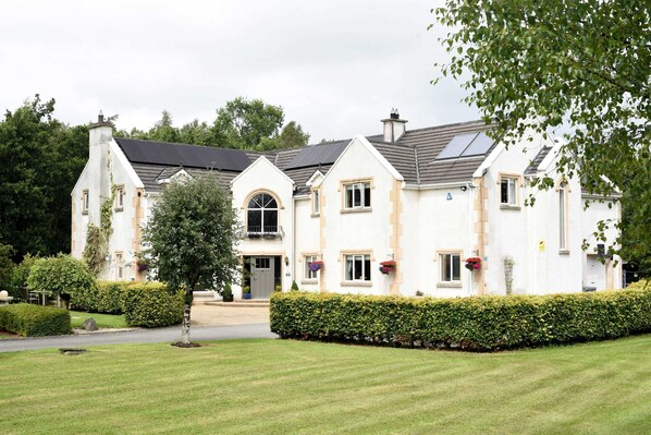 A large, two-story building with a symmetrical facade, multiple windows, and a well-maintained lawn. - Dungimmon House (Ballyconnell)