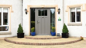 Un bâtiment avec une porte grise, deux plantes en pot de chaque côté et une petite enseigne ornée d’un symbole en forme de cœur et de trois étoiles.