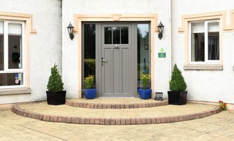 A building with a grey door, two potted plants on either side, and a small sign with a heart symbol and three stars.