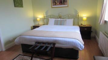 A neatly made bed with a headboard, two bedside tables with lamps, a wooden chair, a floral rug, and a framed picture on the wall.