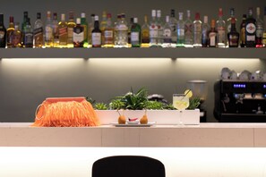 A bar area with a variety of liquor bottles, a fruit bowl with pears and a red chili pepper, and a cocktail glass with a lemon slice. - Brasil Suites Boutique Hotel (Glyfada)