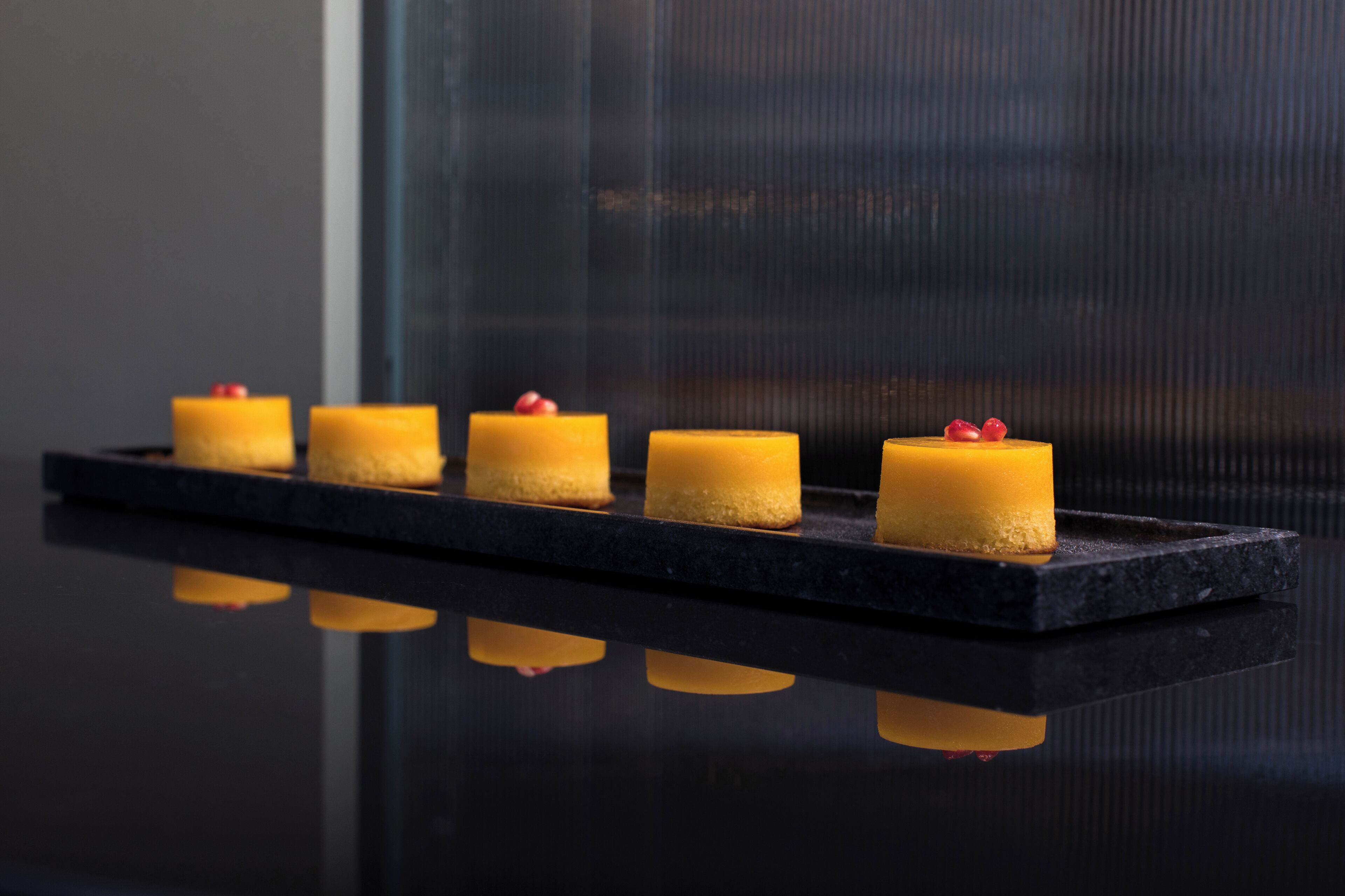 A row of small, square-shaped candles with red berries on top, placed on a black rectangular platform.