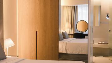 Een hotelkamer met een bed, nachtkastje, lamp, spiegel en een badkamer met een wastafel en handdoekhouder.