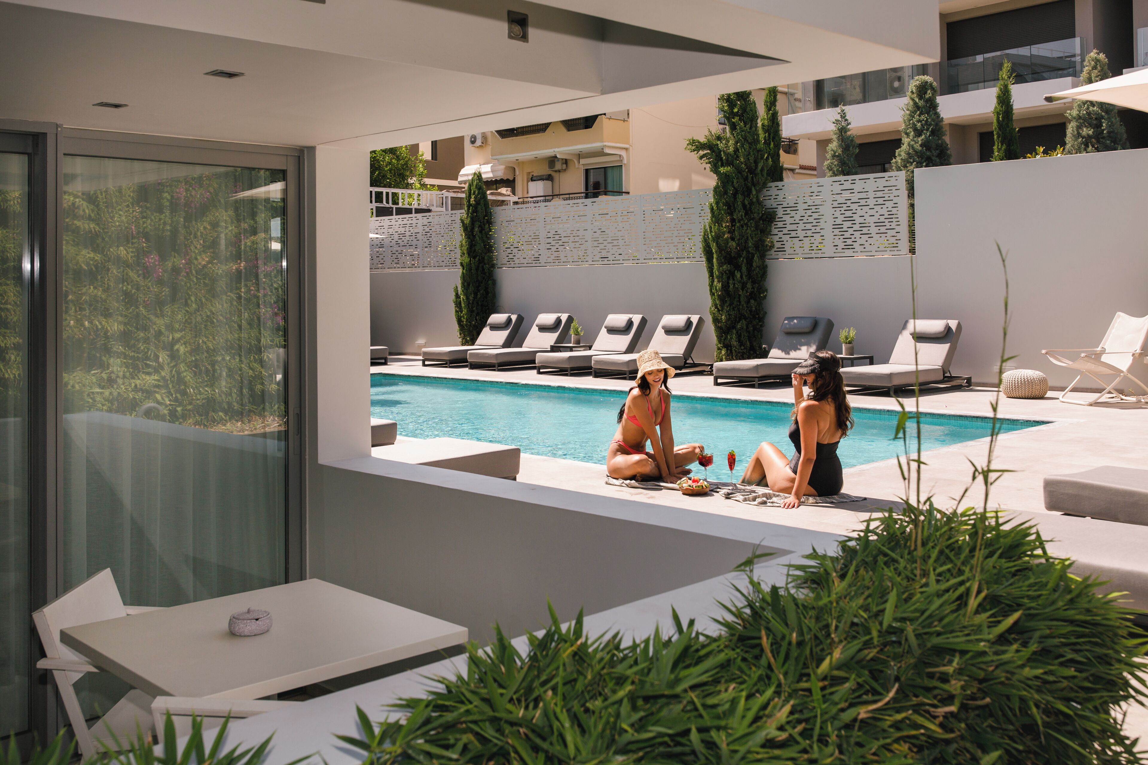 A modern outdoor pool area with lounge chairs and a table, surrounded by greenery.