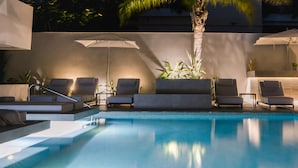 Ein modernes Außenpool-Areal mit Liegestühlen und Sonnenschirmen, umgeben von einem minimalistischen Design und einer Palme.