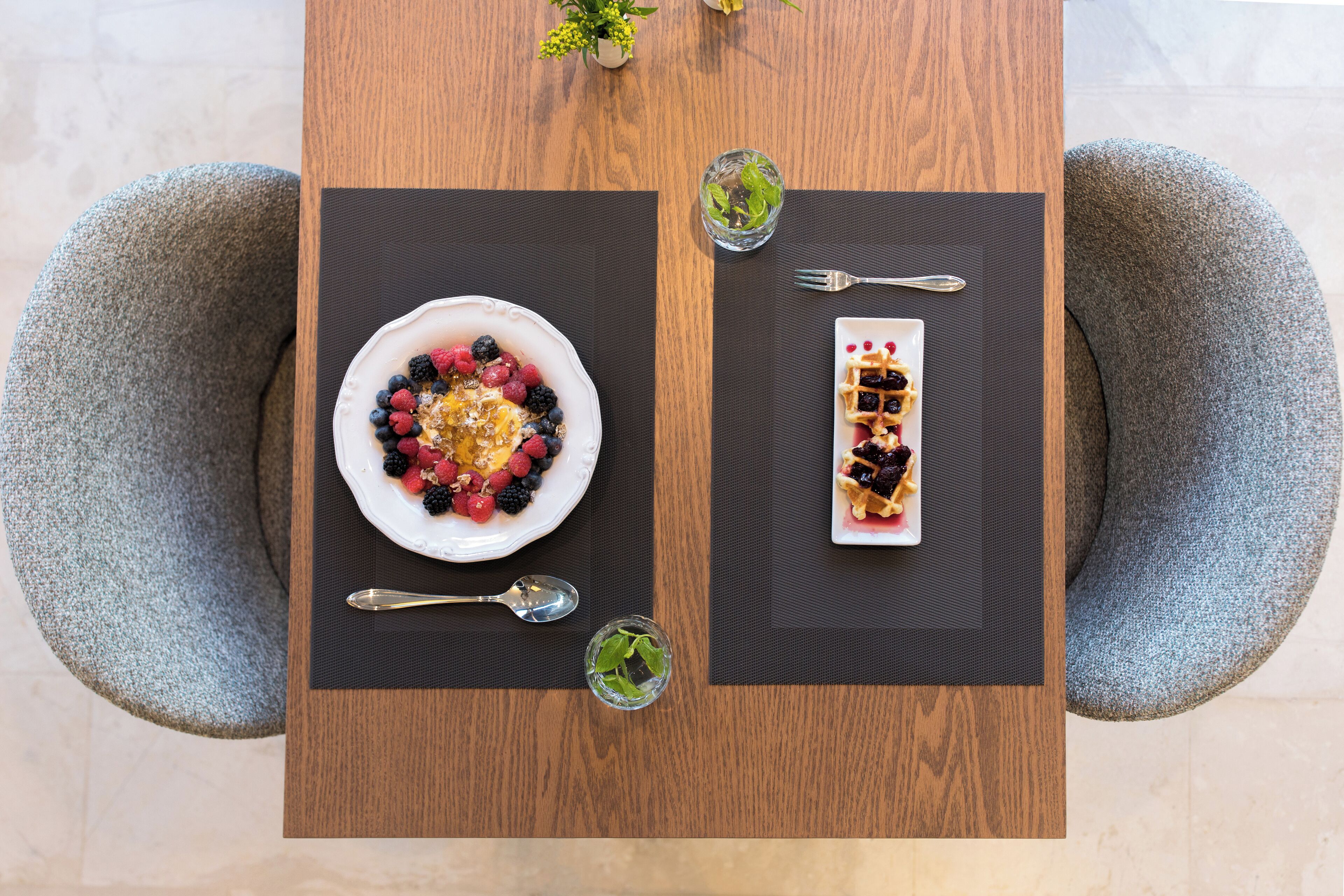 A wooden dining table with two plates of food, two forks, and two glasses of water.