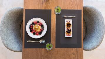 A wooden dining table with two plates of food, two forks, and two glasses of water.