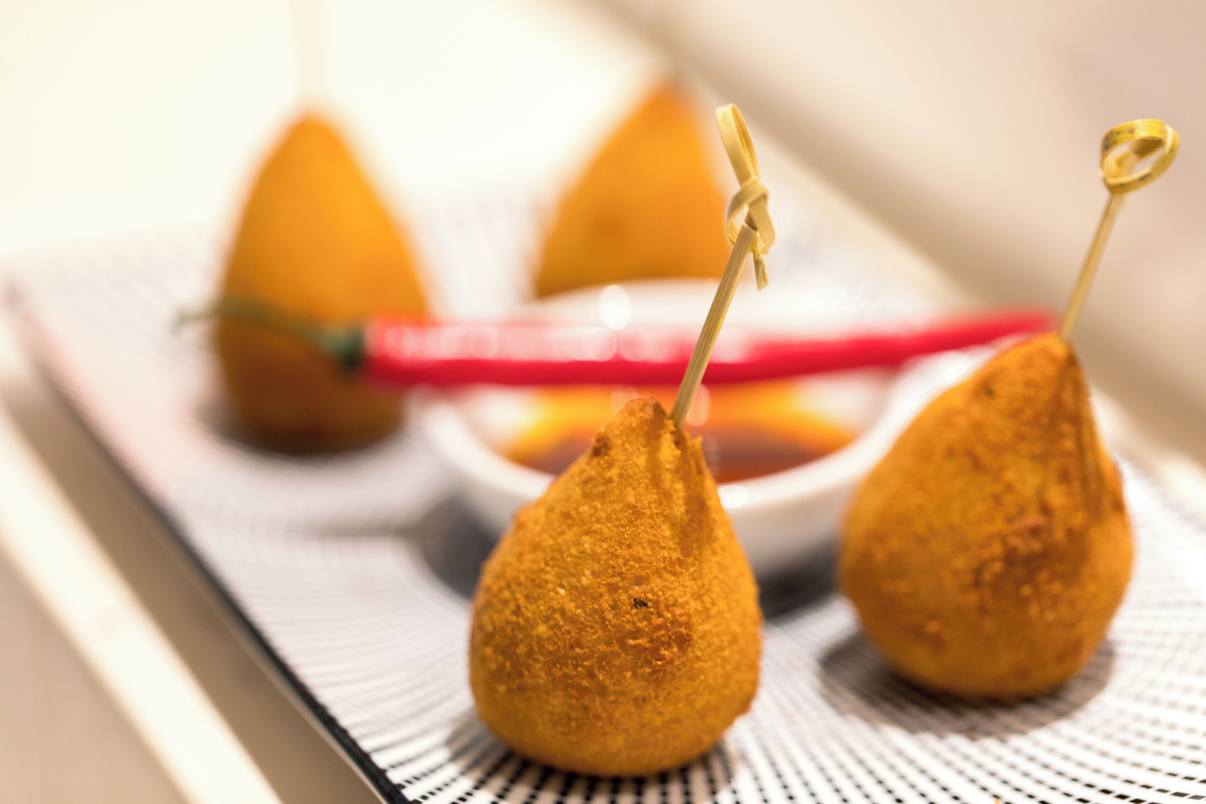 Three golden-brown fried items on a white plate with a red utensil.