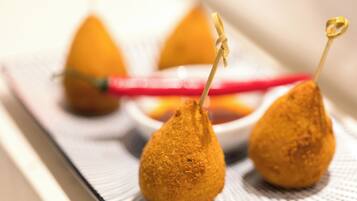 Three golden-brown fried items on a white plate with a red utensil.
