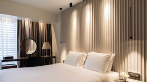 Ein Hotelzimmer mit einem großen Bett, einem Schreibtisch mit Lampe, einem Spiegel und einem Nachttisch mit Blumenvase.