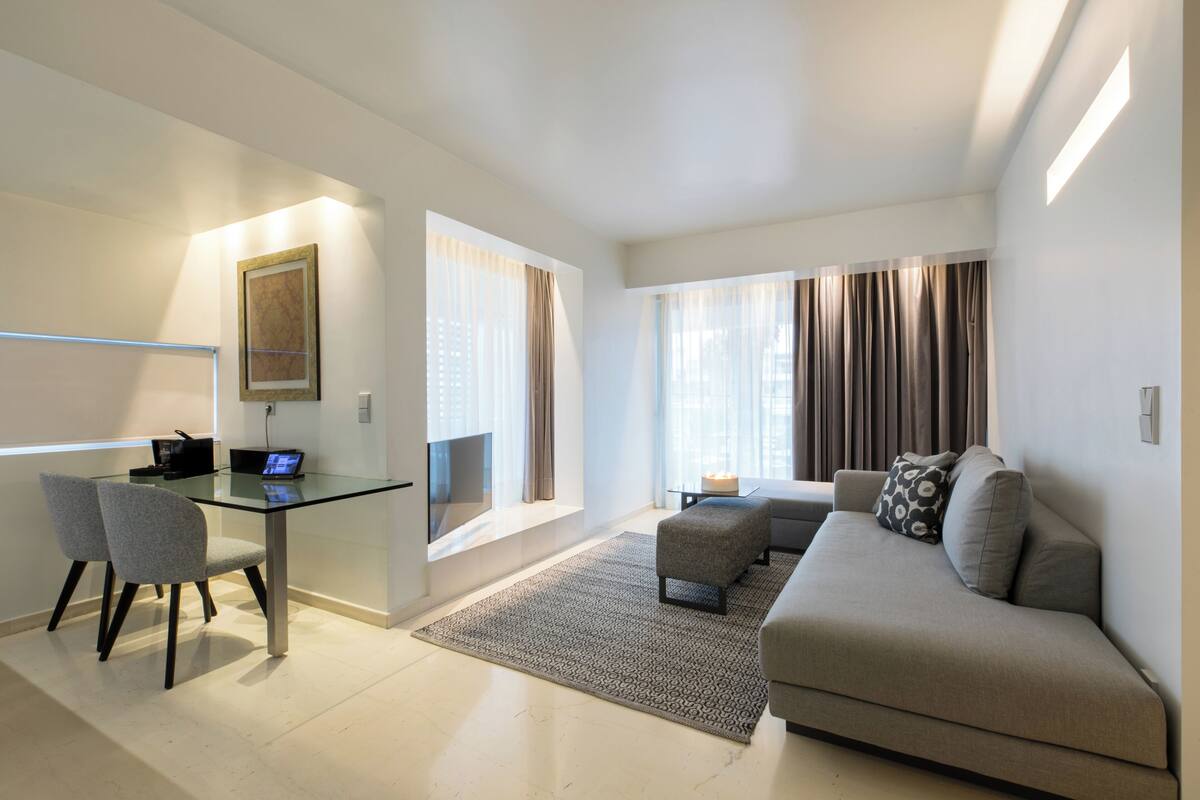 A modern living room with a glass table, two grey chairs, a grey sofa, and a patterned rug.