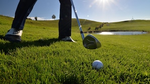 Un campo de golf con cielo despejado, un estanque y una pelota de golf sobre el césped.