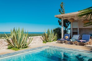 A poolside area with a clear view of the ocean, lounge chairs, and large agave plants. - Riad Tamayourt Ocean View (Essaouira)