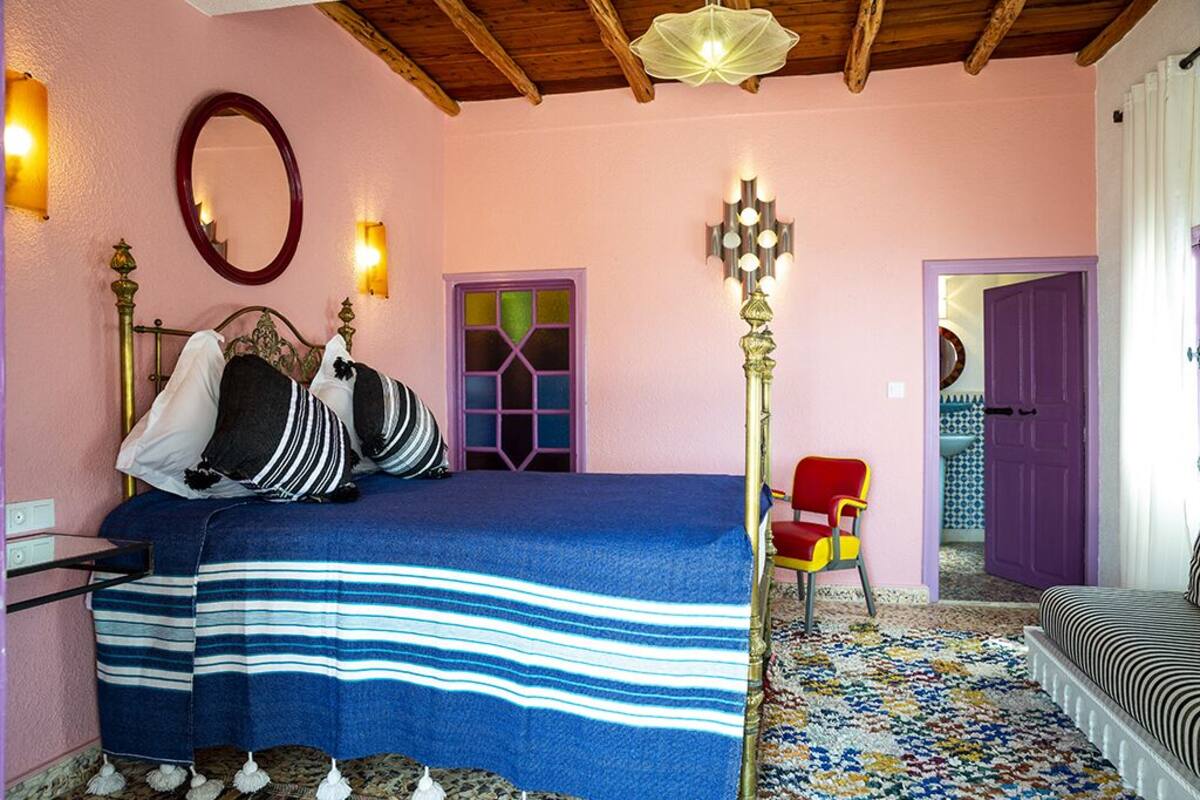 A bedroom with a bed, a chair, a lamp, and a door.