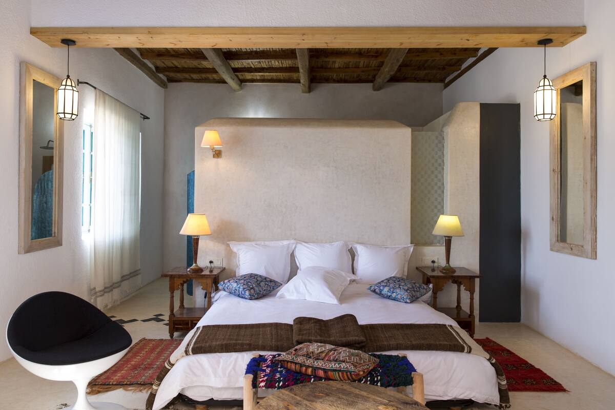 A bedroom with a large bed, two bedside tables with lamps, a chair, and a wooden ceiling.