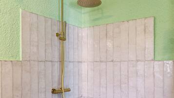 A shower with a gold showerhead and a handheld showerhead, tiled walls, and a geometric tile floor.
