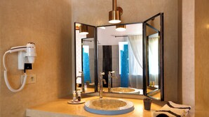 Un baño con un lavabo redondo, un espejo, un secador de pelo y una toalla sobre la encimera.