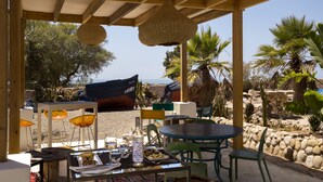 Un patio al aire libre con vigas de madera, luces colgantes de mimbre y una mesa dispuesta con platos, vasos y una botella.