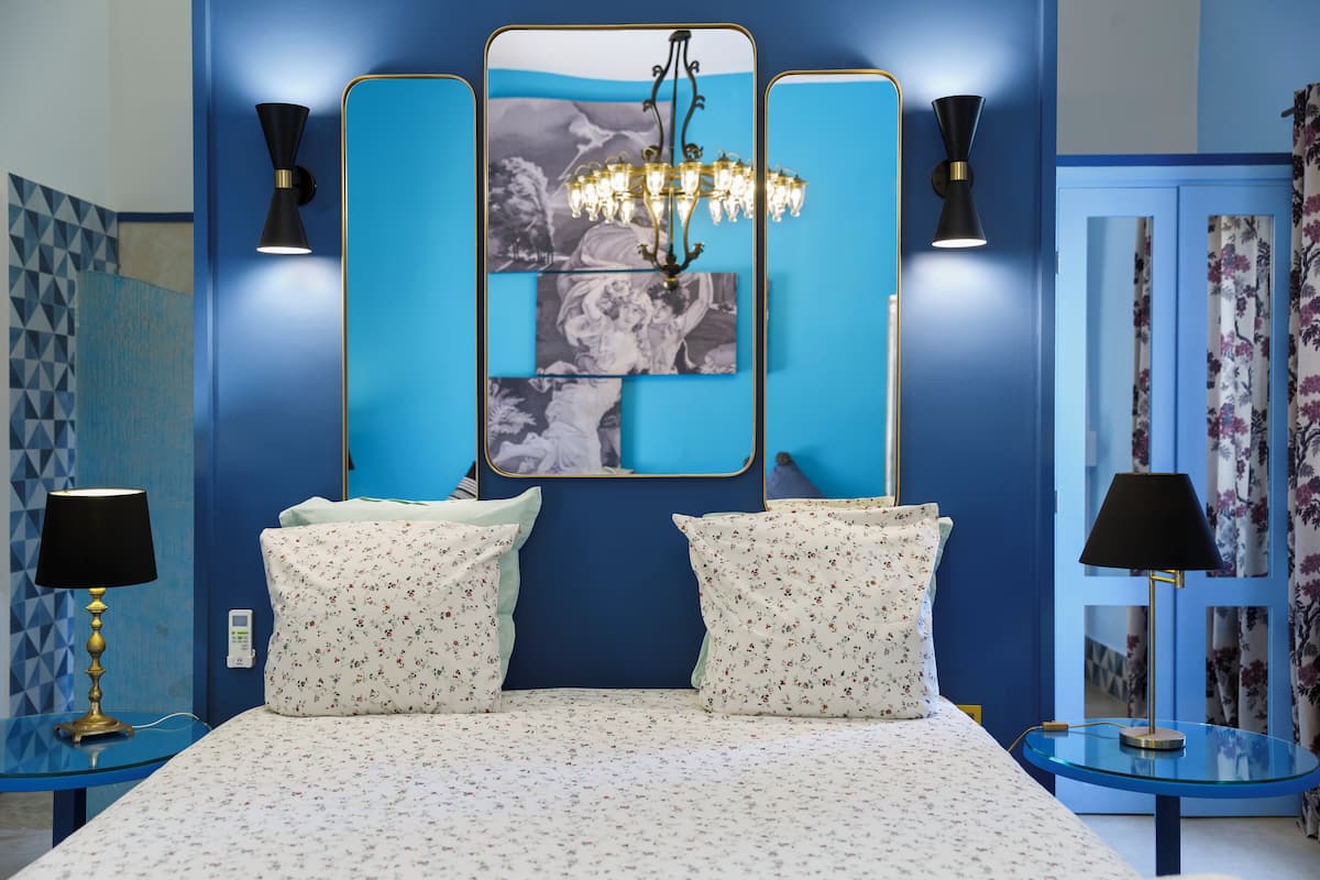 A bedroom with a large bed, two bedside tables with lamps, a chandelier, and a mirror with a floral print.