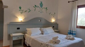 Una cama bien hecha con ropa blanca y almohadas decorativas, una mesita de noche con lámpara y una obra de arte en la pared.