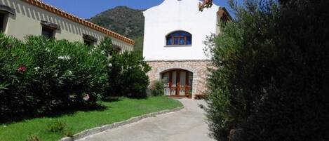 Un edificio con fachada blanca, base de piedra y puerta roja. Un sendero conduce a la entrada.