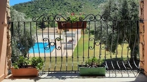 Un balcón con una reja de hierro forjado, una piscina y un paisaje montañoso al fondo.