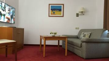 Una sala de estar con televisor, un sofá, una mesita con una planta y un cuadro en la pared.