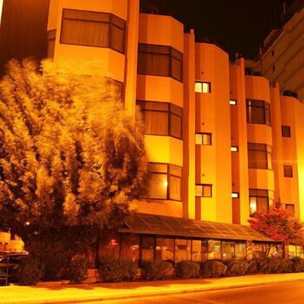 Un hotel de varios pisos con diseño moderno, que cuenta con un gran árbol en la parte frontal y un espacio al aire libre cubierto.
