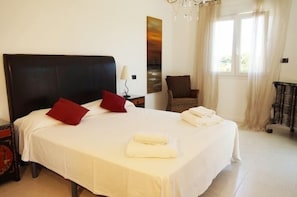 Uma cama bem arrumada com lençóis brancos e almofadas vermelhas, uma cabeceira preta e uma mesa de cabeceira com um abajur.