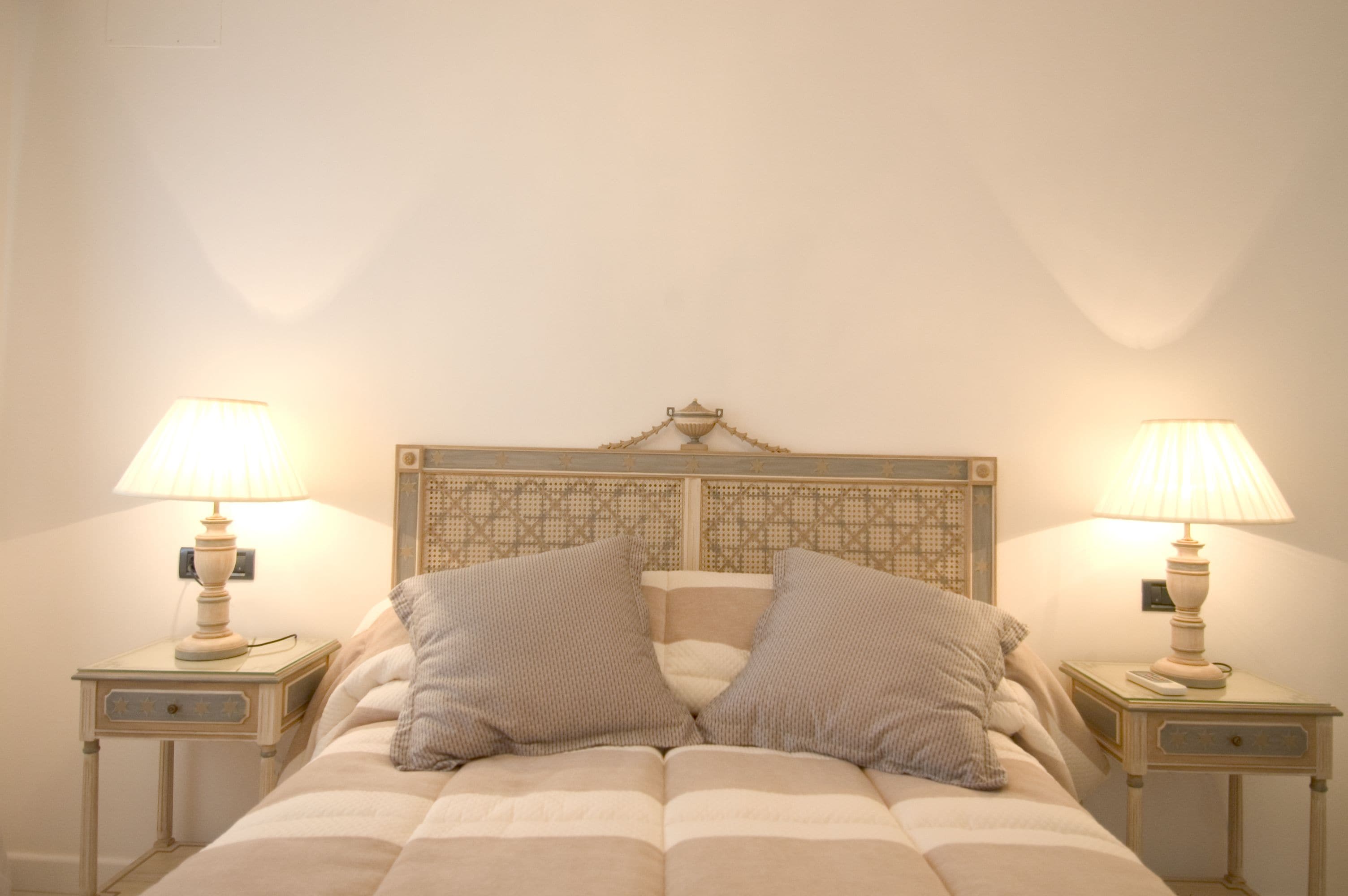 Una cama con cabecera, dos mesitas de noche con lámparas y dos almohadas.