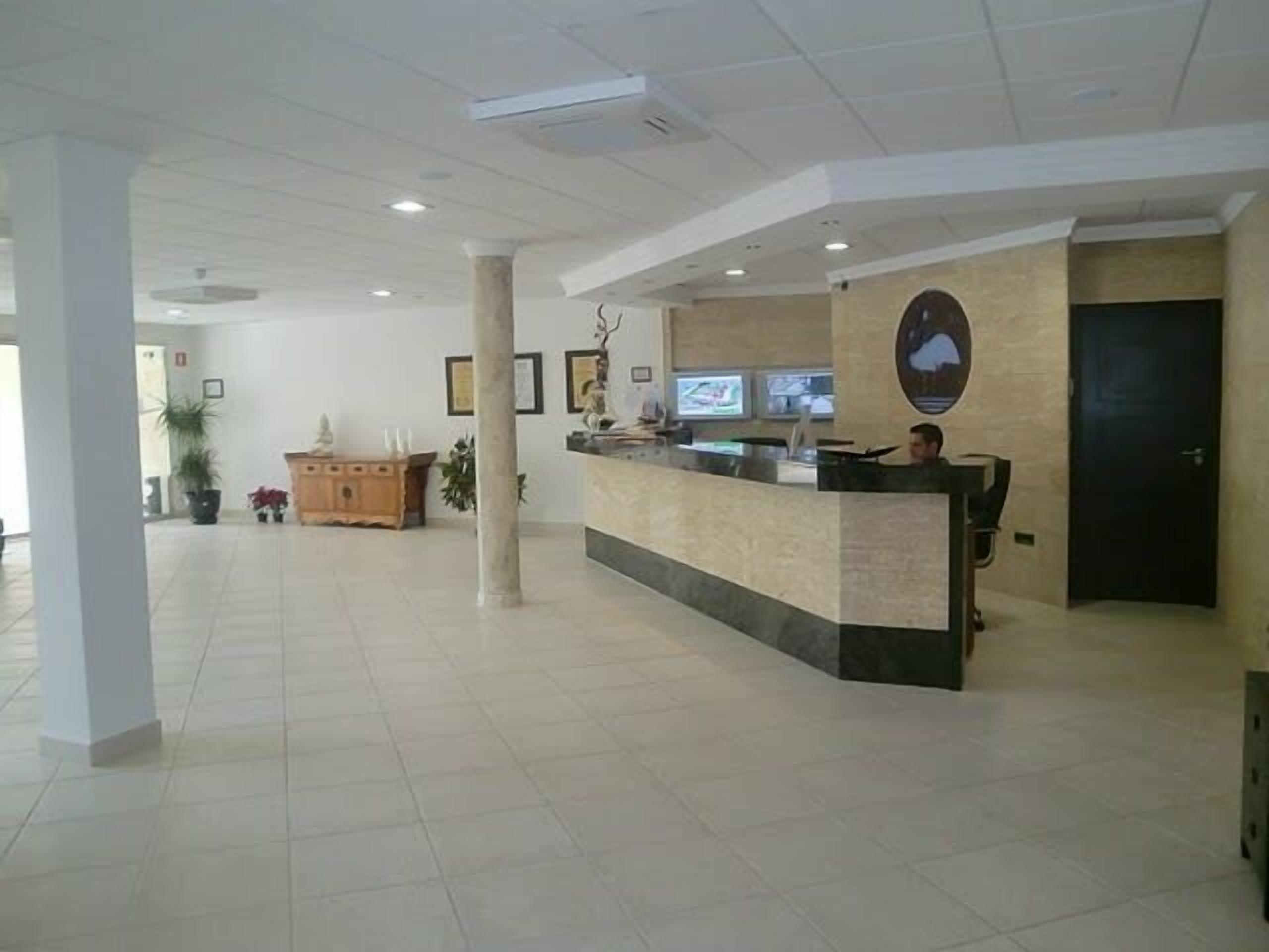 A reception area with a reception desk, a wooden cabinet, potted plants, and a large pillar.