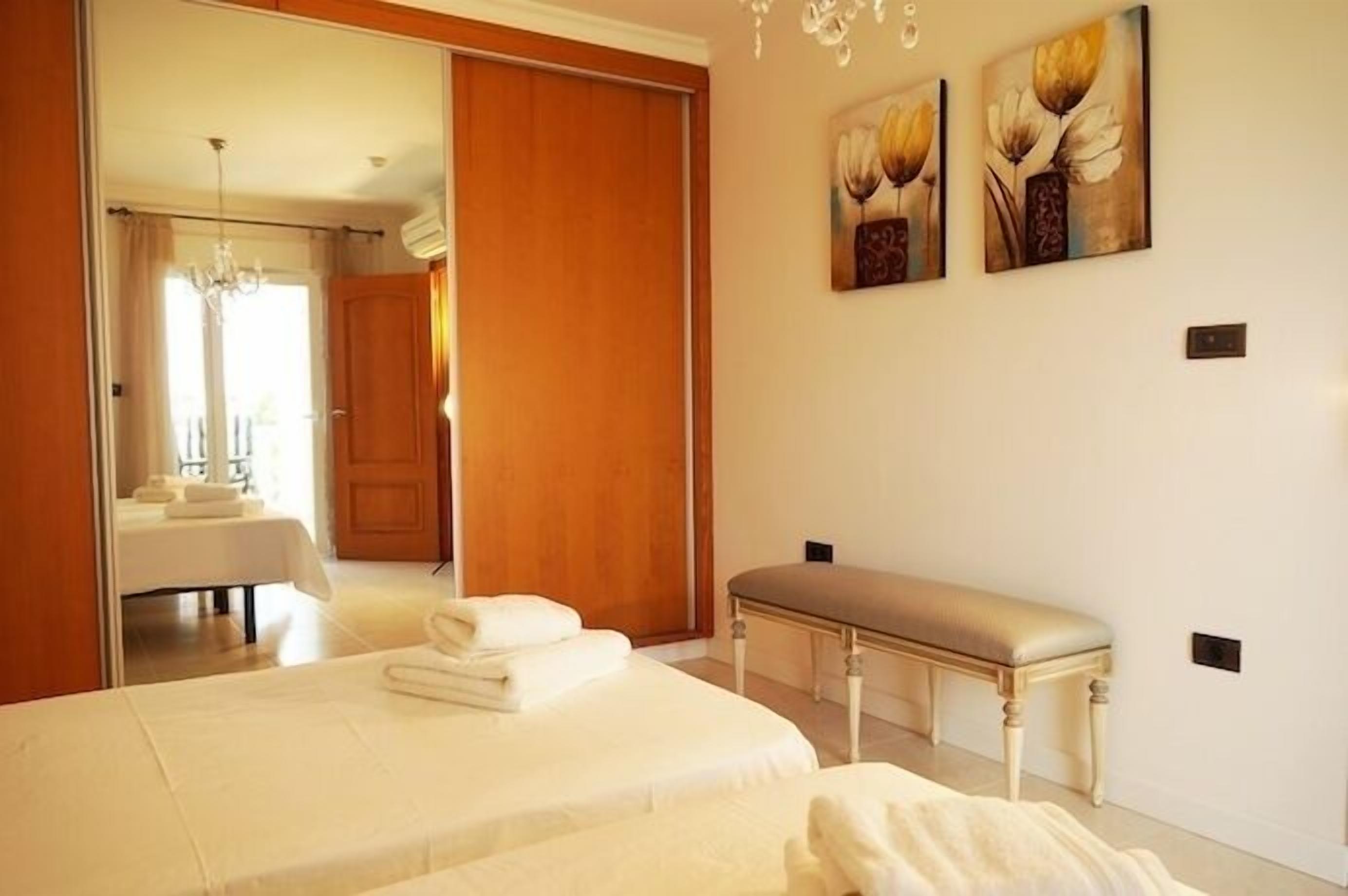 Un dormitorio con una cama grande, un banco y dos cuadros en la pared.