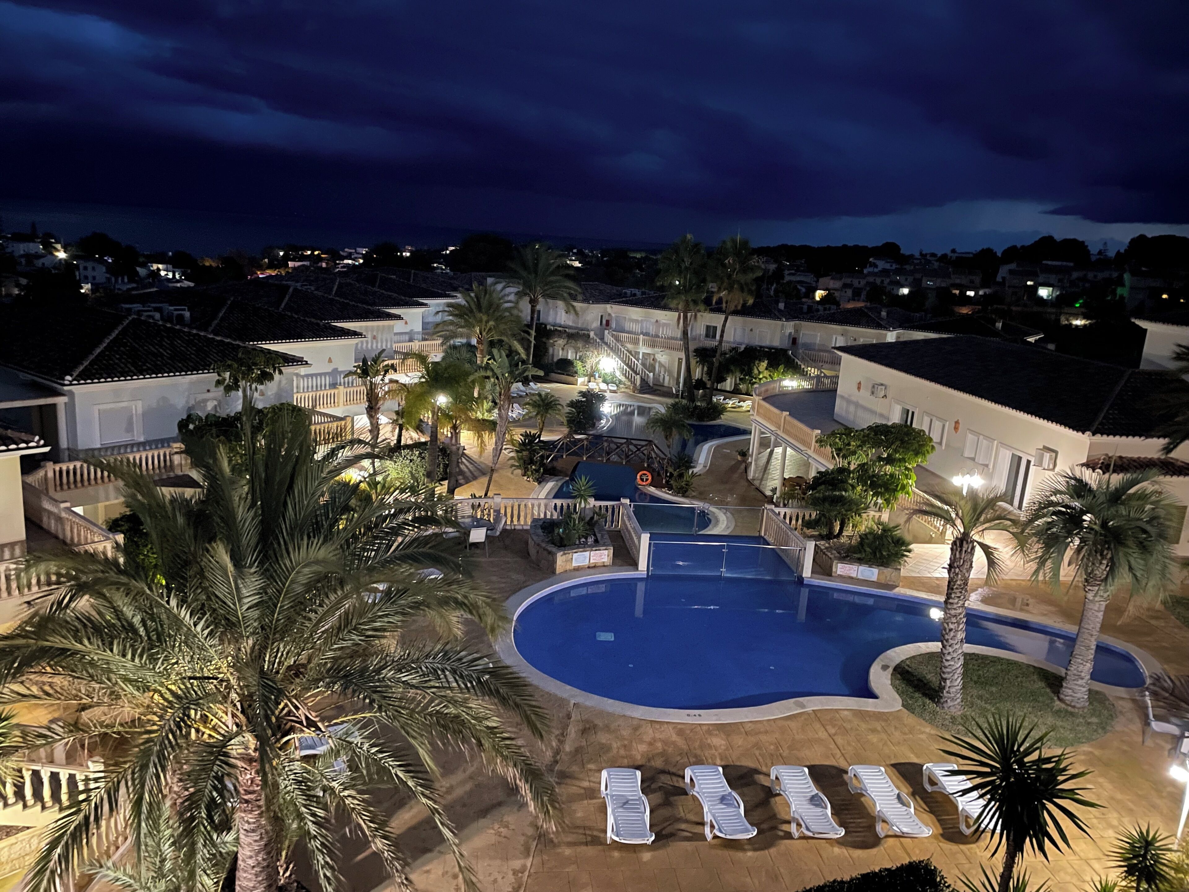 Un resort con piscina, palmeras y vista del barrio circundante por la noche.