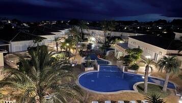 Un resort con piscina, palmeras y vista del barrio circundante por la noche.
