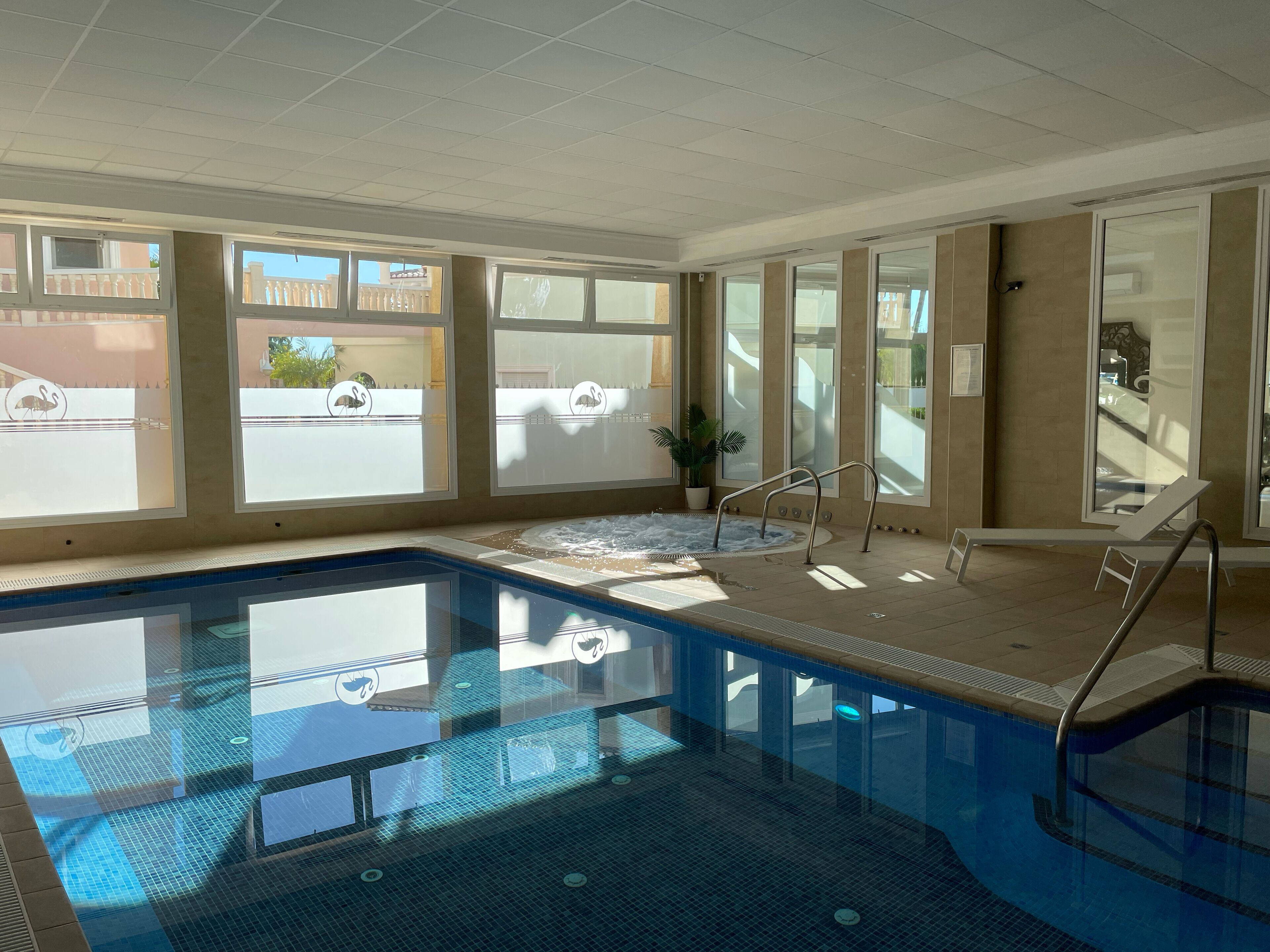 Une piscine à l’eau d’un bleu cristallin, un intérieur baigné de lumière et de grandes fenêtres offrant une vue sur l’extérieur.