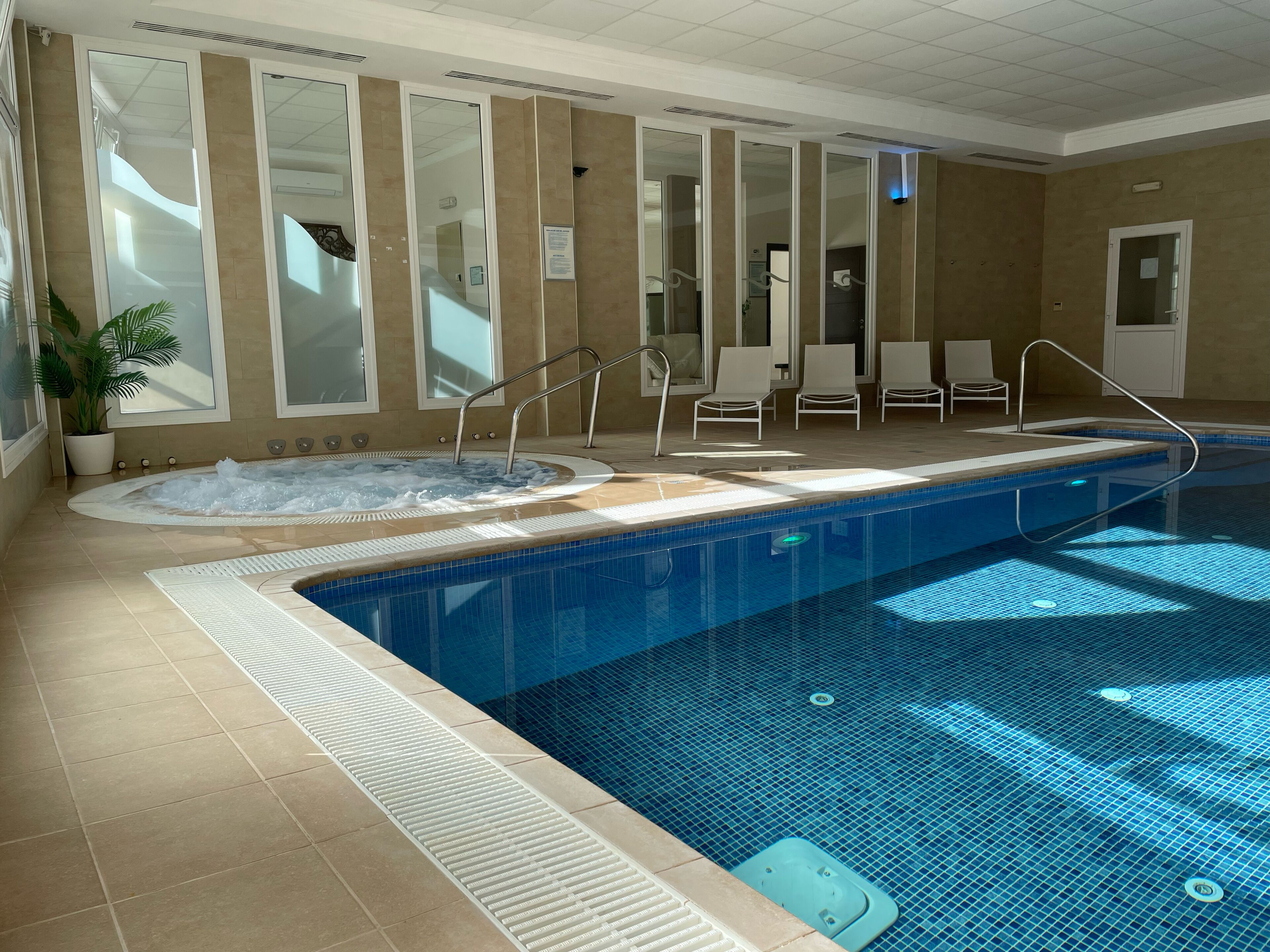 Una piscina interior con un jacuzzi, sillas de descanso y una planta en maceta.