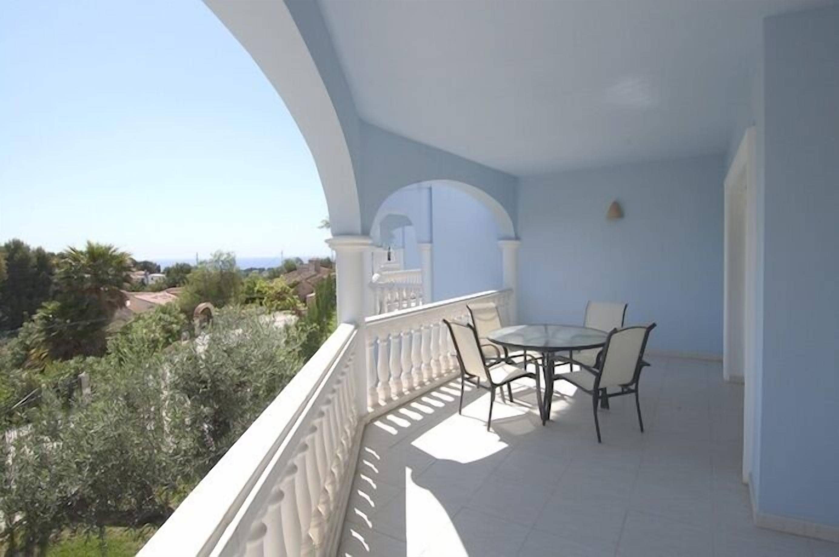 A balcony with a table and chairs, white balustrade, and a view of greenery and buildings.