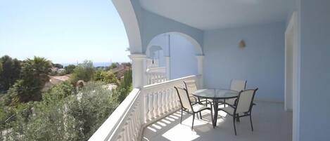 A balcony with a table and chairs, white balustrade, and a view of greenery and buildings.