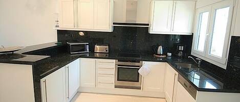 A modern kitchen with white cabinets, black countertops, and stainless steel appliances.