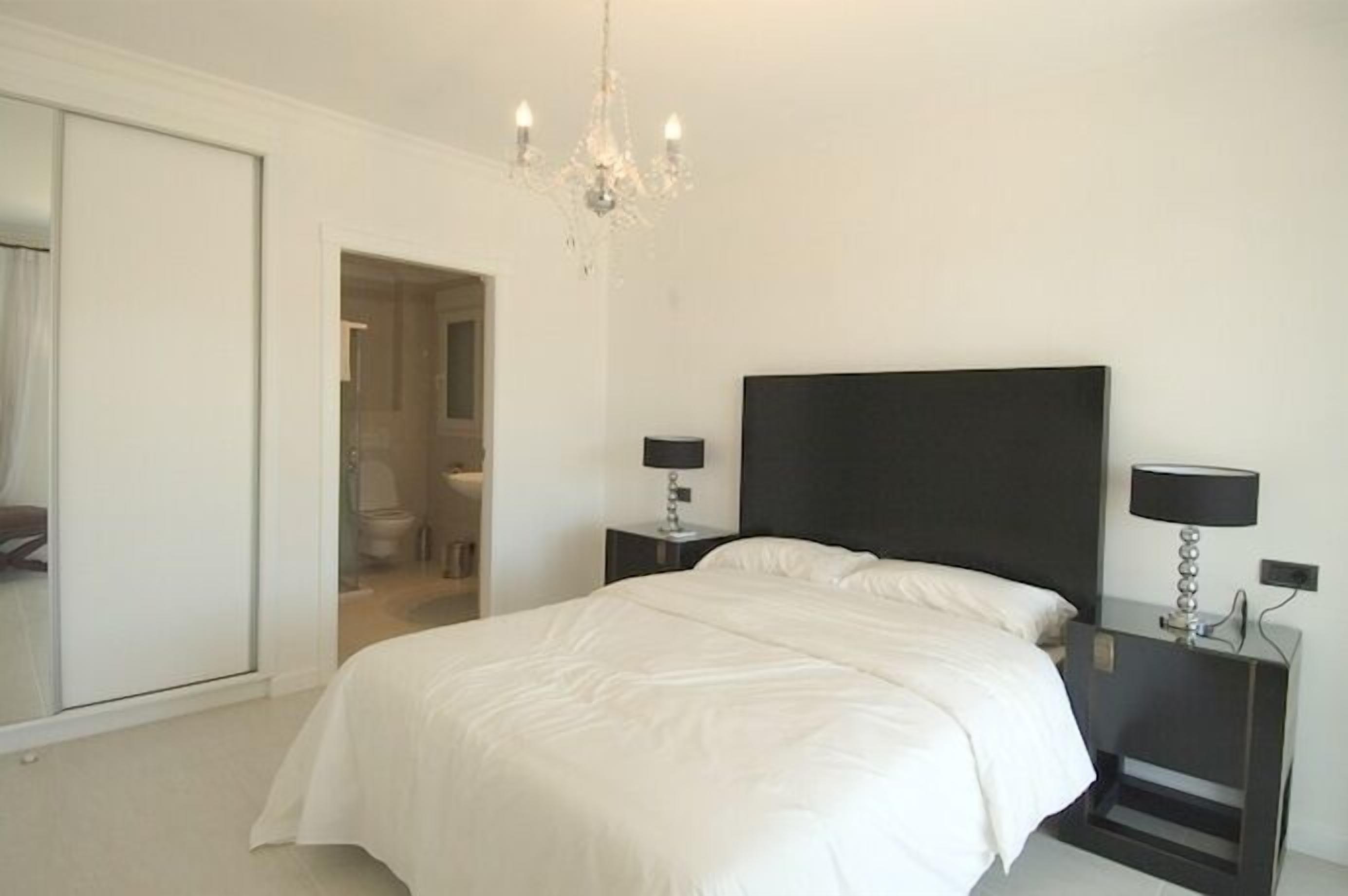 A bedroom with a large bed, a chandelier, and two bedside tables with lamps.